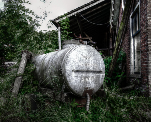 an old dirty white water tank abandoned in the middle of wild plants and a house