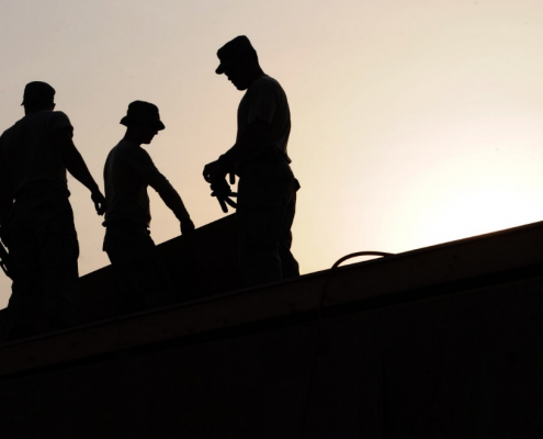 Silhouette of three workers wearing safety caps while working